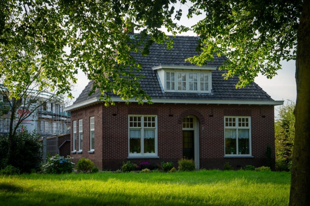 A quaint brick house surrounded by a lush green yard and trees in a suburban setting.