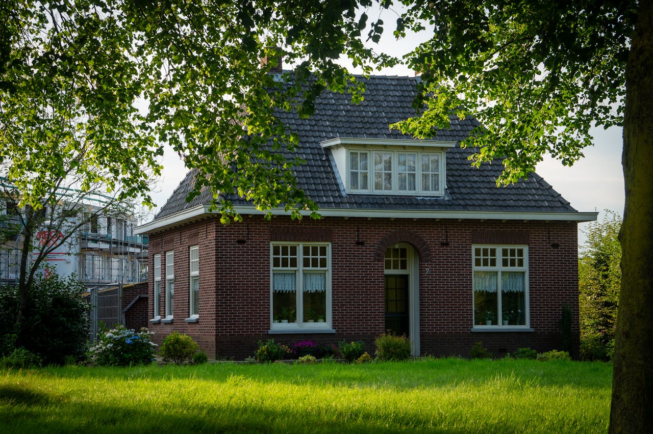 A quaint brick house surrounded by a lush green yard and trees in a suburban setting.