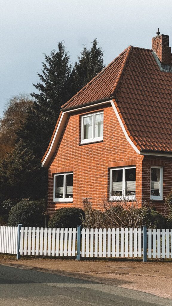 A cozy red brick house with a white picket fence under a clear sky.